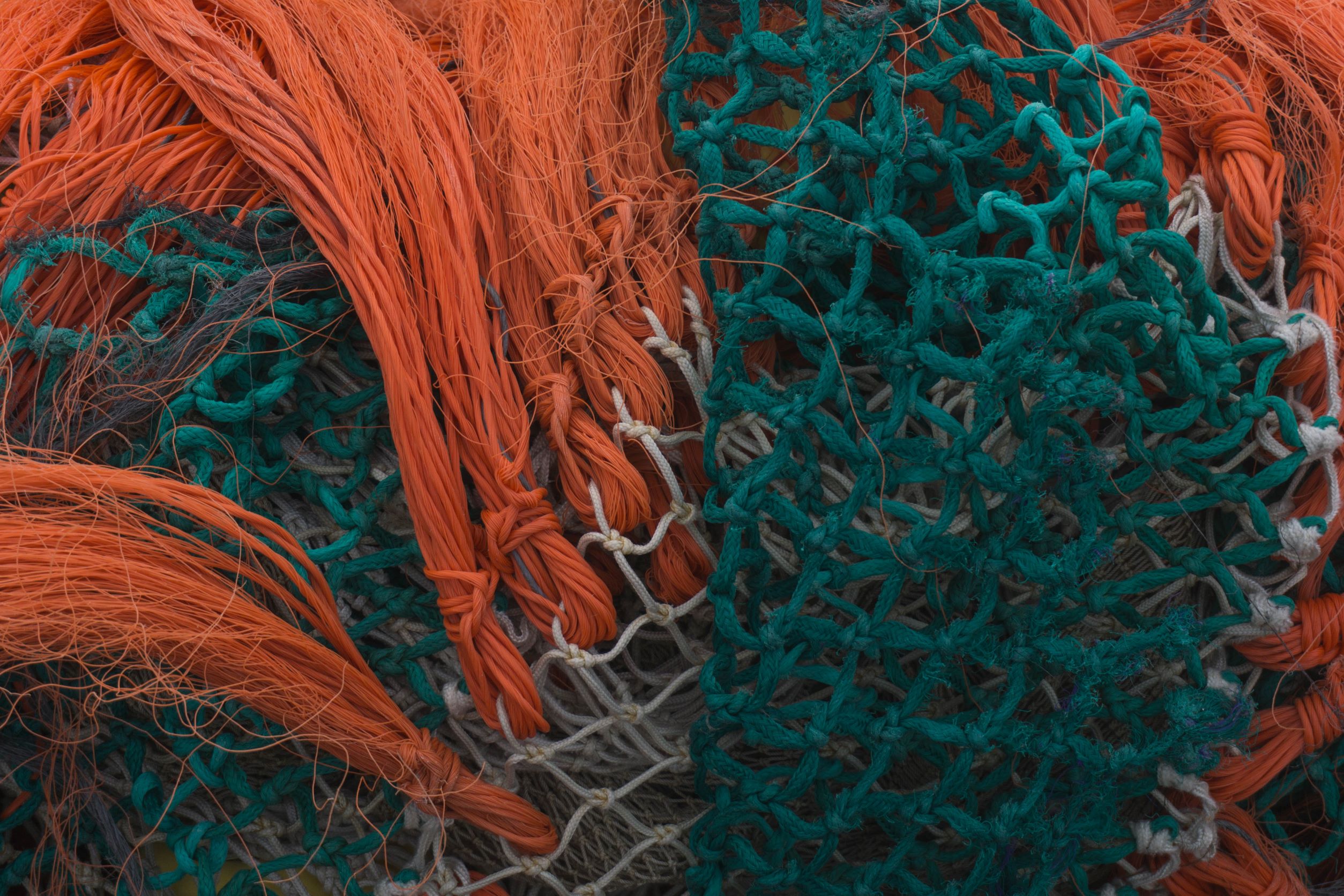 Das Bild zeigt ineinander verknotete Fischernetze in den Farben orange, weiß und grün.